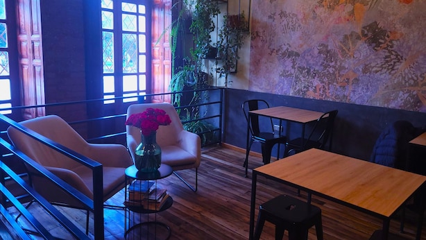 A cozy cafe with wooden furniture, a vase of red roses, and a rustic wall. - Sun Backpackers (Quito)