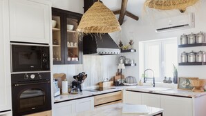 A modern kitchen with white cabinetry, a black oven, a hanging woven light fixture, and a built-in stove. - Casa Vó Briata (Mértola)