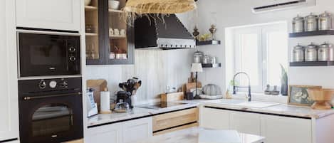 A modern kitchen with white cabinetry, a black oven, a hanging woven light fixture, and a built-in stove.