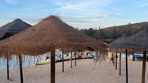 A beach with thatched umbrellas and a sandy area. - Casa Vó Briata (Mértola)
