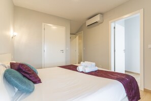 A hotel room with a bed, a bathroom door, and an air conditioning unit.