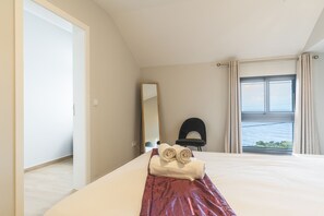 Une chambre d’hôtel avec un lit, une chaise, une grande fenêtre donnant sur un beau paysage et un miroir au mur.