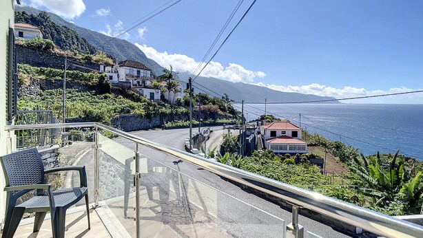 Ein Balkon mit Blick auf eine Küstenstraße, Häuser und das Meer.