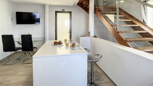 Ein modernes Hotelzimmer mit einer weißen Rezeption, einem Flachbildfernseher, einer Treppe mit Holzwangen und einer Glastrennwand.