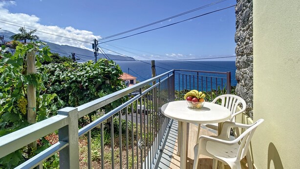 Ein Balkon mit Tisch und Stühlen, der Blick auf die Küste mit Bergen im Hintergrund freigibt.