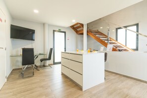 Una cocina moderna con una escalera de madera, un comedor con mesa de vidrio y un televisor de pantalla plana montado en la pared.