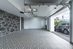A covered parking area with a patterned floor, a stone wall, and a car parked outside.