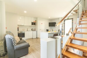 A modern apartment with a kitchenette, a dining area, a living room with a sofa, and a wooden staircase.