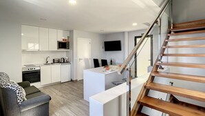 Eine moderne Küche mit weißen Schränken, einer Mikrowelle und einem Einbauofen. Es gibt einen Essbereich mit einem weißen Tisch und Stühlen, sowie eine Holztreppe, die zu einer anderen Ebene führt.