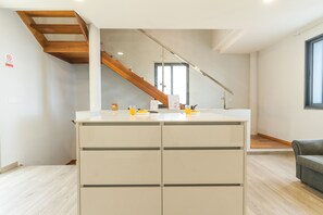 A modern kitchen with a central island, a wooden staircase, and a view of the living area.