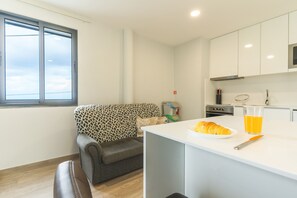 A modern kitchen with a dining area, a sofa, a coffee machine, and a glass of orange juice on the counter.