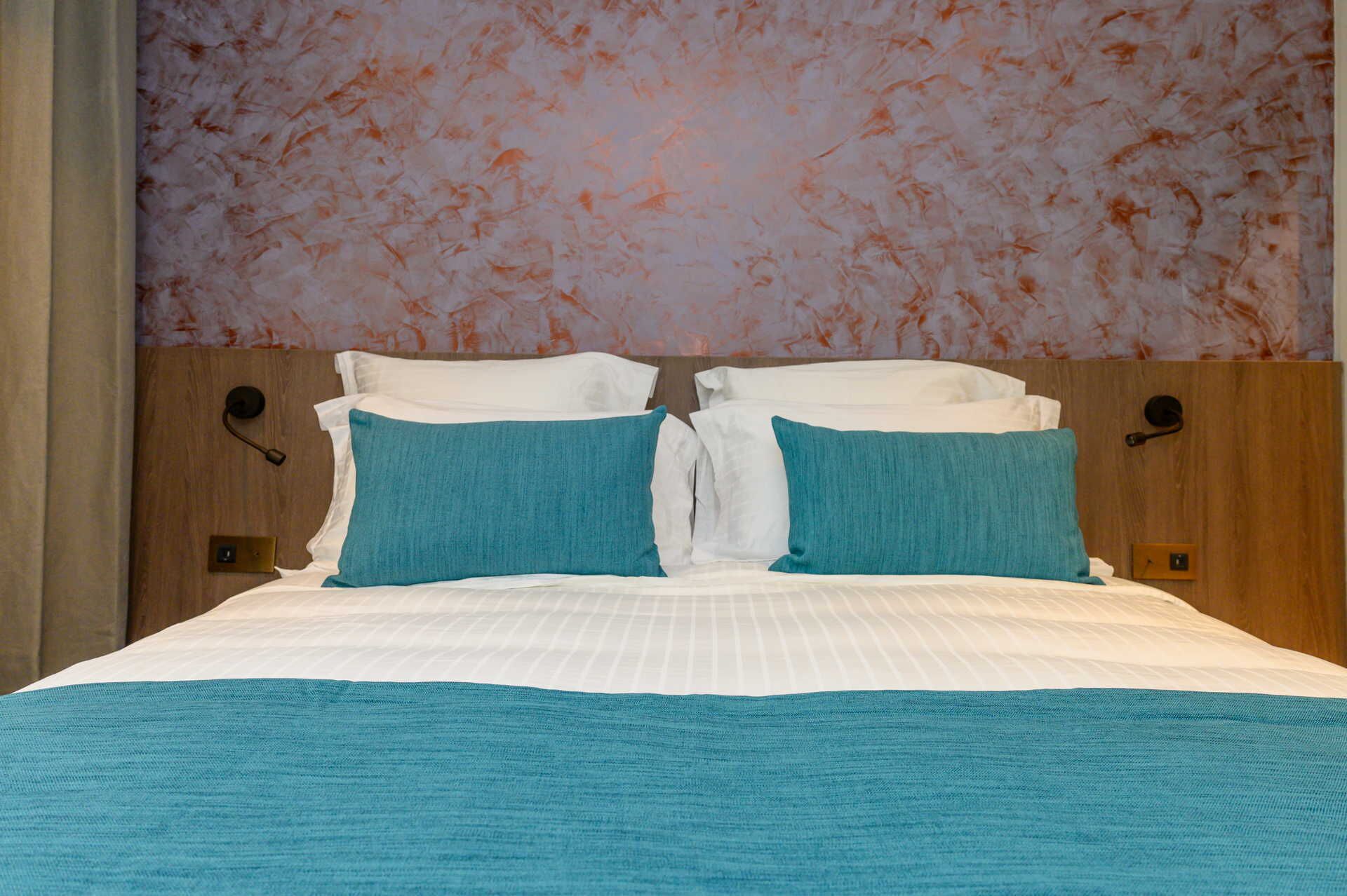 A hotel room with a bed, two pillows, a headboard, and a wall with a floral pattern.