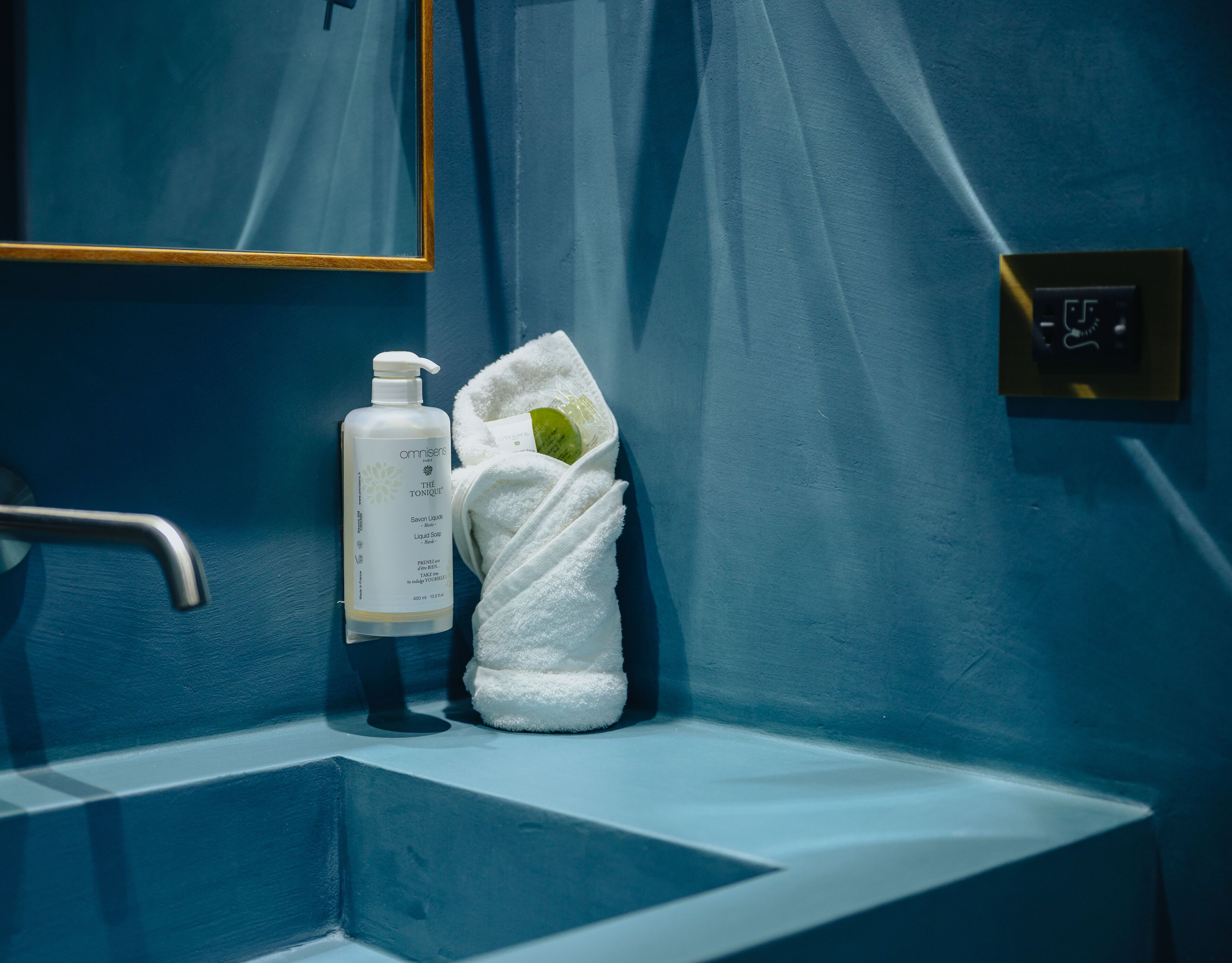 Un baño con un lavabo azul, una botella de jabón y una toalla.
