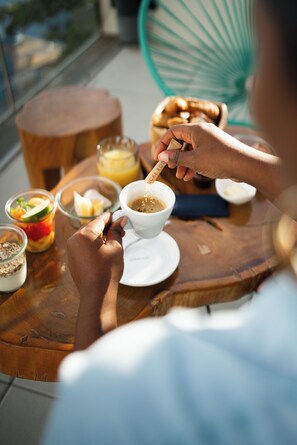 A person sitting at a wooden table with a cup of coffee, a bowl of fruit, and a glass of orange juice. - SABLE BLEU BOUTIQUE HOTEL (Le Marin)