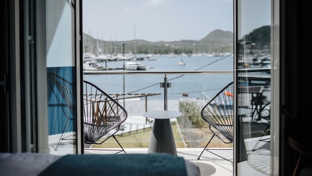 A balcony with two wire-framed chairs and a small round table, overlooking a marina with boats and a hilly landscape. - SABLE BLEU BOUTIQUE HOTEL (Le Marin)