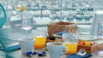 A breakfast table with a view of a marina, a woven bag, and various breakfast items.