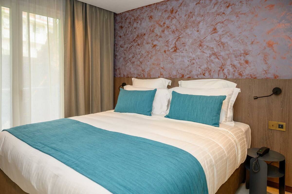 A hotel room with a large bed, a wooden headboard, a nightstand, and a wall with a textured pattern.