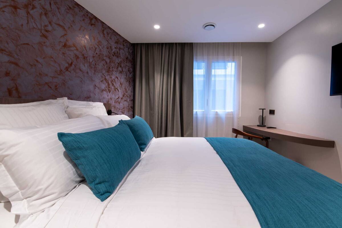 A modern hotel room with a large bed, a desk, and a view of the outdoors.