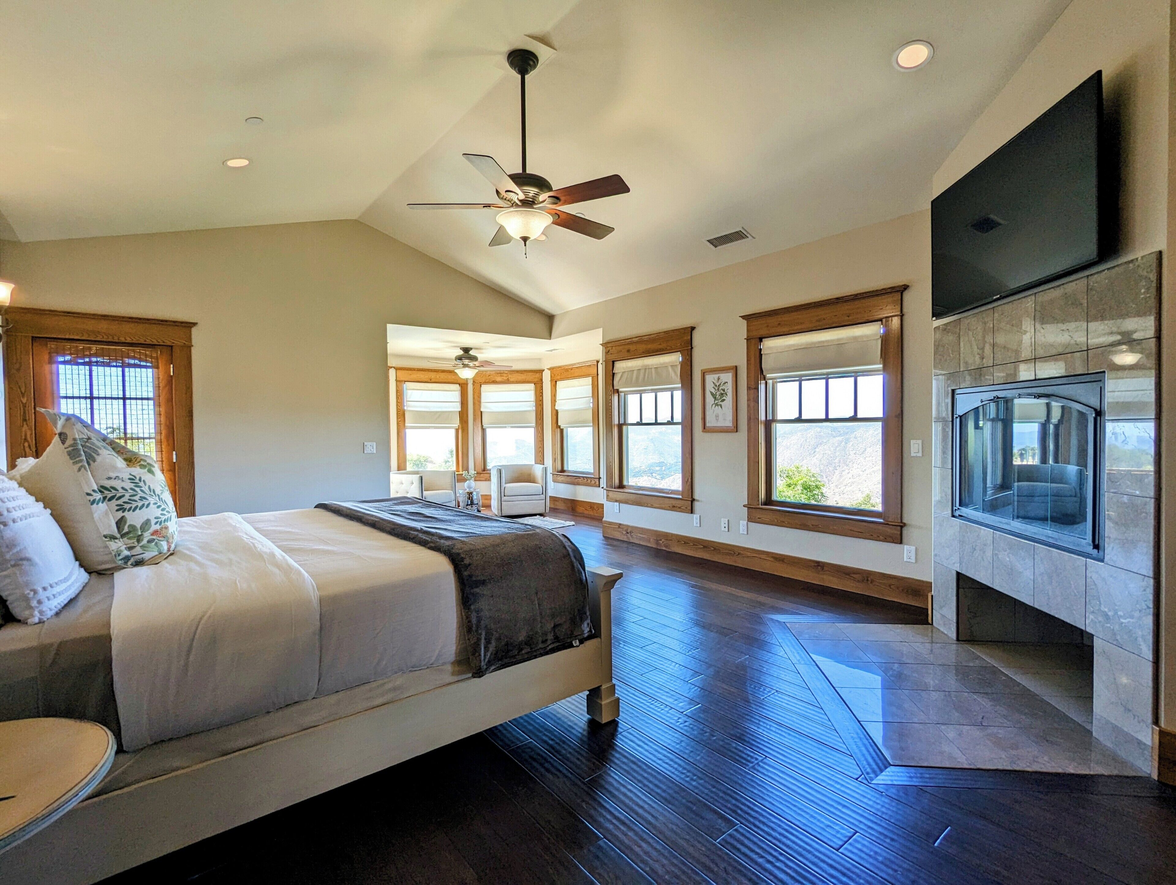 A spacious bedroom with a large bed, a ceiling fan, and a fireplace.