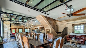 Un vaste espace dédié à la salle à manger, avec une grande table en bois et des chaises en cuir, un lustre et un escalier menant à une mezzanine.