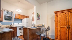 A kitchen with wooden cabinets, a white stove, a bar area with two bar stools, and a large wooden cabinet. - Historic Oregon District (Dayton)