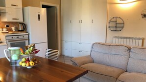 Un espacio habitable pequeño con kitchenette, una mesa de comedor con frutas, un sofá y un radiador.