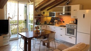 Una cocina moderna con gabinetes blancos, una estufa a gas y un horno empotrado. Hay una mesa de comedor con sillas y un sofá en la sala.