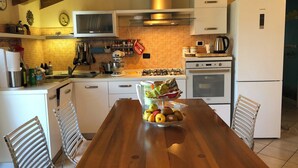 Una cocina con armarios blancos, una mesa de madera con fruta y un microondas sobre la estufa.