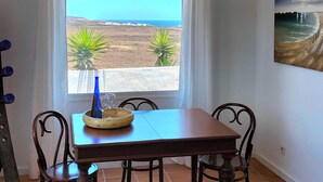 Una zona de menjador amb vista al mar, una taula amb cadires, una làmpada penjant i un quadre a la paret.