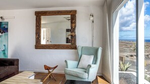 Habitació amb una finestra gran, una butaca blau clar, un mirall amb marc de fusta i vista a un paisatge desèrtic.