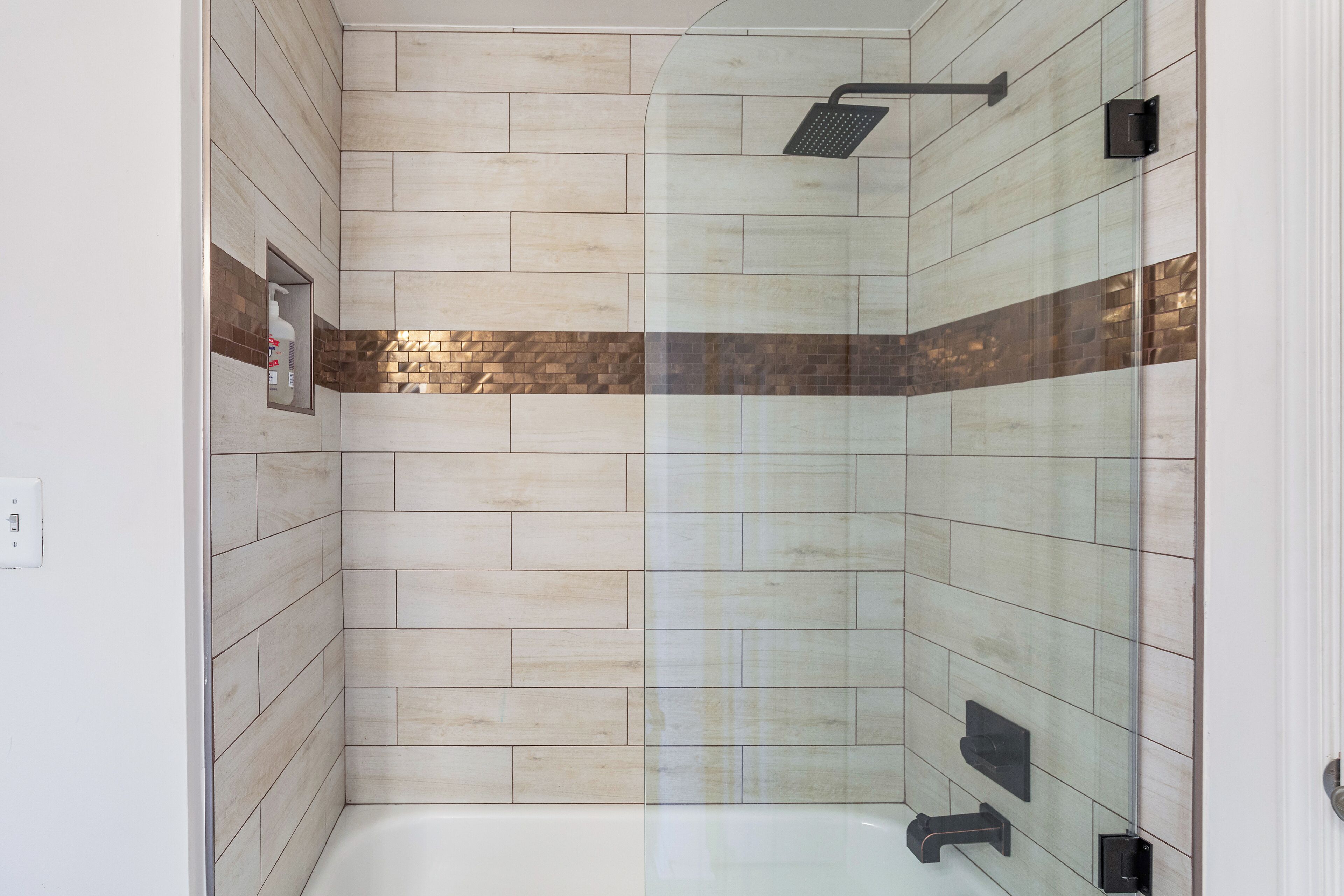 Un espace douche moderne doté d’une porte en verre, d’un pommeau de douche à main et d’un panneau de commande fixé au mur.