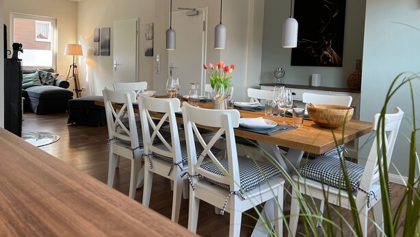 Uma sala de jantar moderna com mesa de madeira, cadeiras brancas e luminárias pendentes.