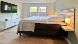 A modern bedroom with a bed, bedside table, lamp, and a TV on the wall. - House on the mountain - 150sqm duplex apartment (Braunlage)
