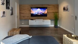 Uma sala de estar moderna com uma televisão de tela plana fixada em uma parede de madeira, um sofá, uma mesinha lateral e um vaso de planta.