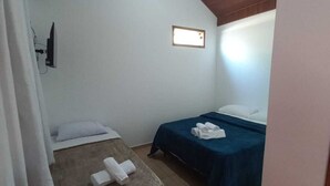 A small, single-room accommodation with a wooden ceiling, a ceiling fan, a bed with a blue bedspread, and a small bedside table with towels. - São Pedro da Serra (Nova Friburgo)