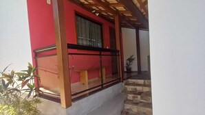 A covered outdoor area with a red wall, a wooden balcony, and a stone-tiled floor. - São Pedro da Serra (Nova Friburgo)