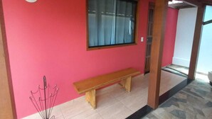 A room with a red wall, a wooden bench, a window with curtains, and a tiled floor. - São Pedro da Serra (Nova Friburgo)
