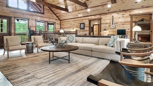 Interior acogedor de una cabaña con techo de madera, un sofá grande, una mesa de centro y un comedor.
