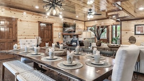 Un interior de madera con una larga mesa de comedor dispuesta con tazas blancas y posavasos, una chimenea y un ventilador de techo.
