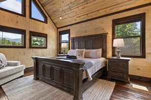 A bedroom with a large bed, a nightstand, a chair, and multiple windows.