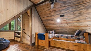 A cozy loft bedroom with a sloped ceiling, wooden walls, a built-in bed, a small seating area, and a window providing a view of the outdoors. - Lakefront Cabin + Dock + Mountain Views (Cherry Log)