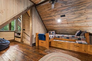 Ein Schlafzimmer im Loft-Stil mit holzverkleideter Schräge, einem integrierten Bett mit Karo-Bettwäsche, einem kleinen Holztisch und einem Sitzsack.