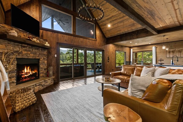 A spacious living room with a stone fireplace, leather sofas, and large windows offering a view of the outdoors.