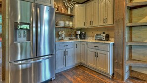 A kitchen with stainless steel appliances, wooden cabinets, and a rustic wooden floor. - Lakefront Cabin + Dock + Mountain Views (Cherry Log)