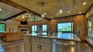 Un'ampia cucina con un'isola grande, soffitto in legno e ampie finestre che offrono vista sull'esterno.