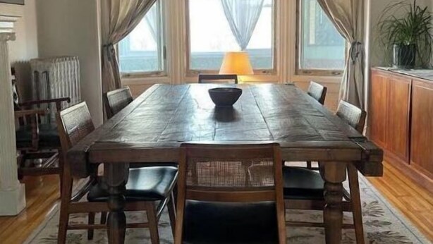 Ein Esszimmer mit einem großen Holztisch, sechs Stühlen, einer Kristallleuchter und Blick auf das Meer durch große Fenster.