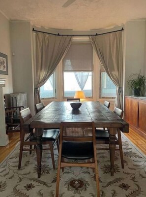 A dining room with a large wooden table, six chairs, a chandelier, and a view of the sea through large windows. - Beautiful Victorian Home (Newark)