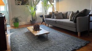 Ein Wohnzimmer mit grauem Sofa, einem Couchtisch, einer Topfpflanze und einem Gemälde an der Wand.