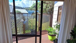 A view through a sliding glass door to an outdoor deck with a wooden floor, a lattice fence, and potted plants. - Comfort and the best seat in the west to view the Tasman Sea (Baylys Beach)