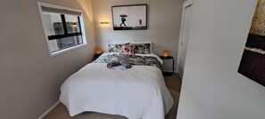 Une chambre à coucher avec un lit, une fenêtre, un tableau et une table de chevet avec une lampe.